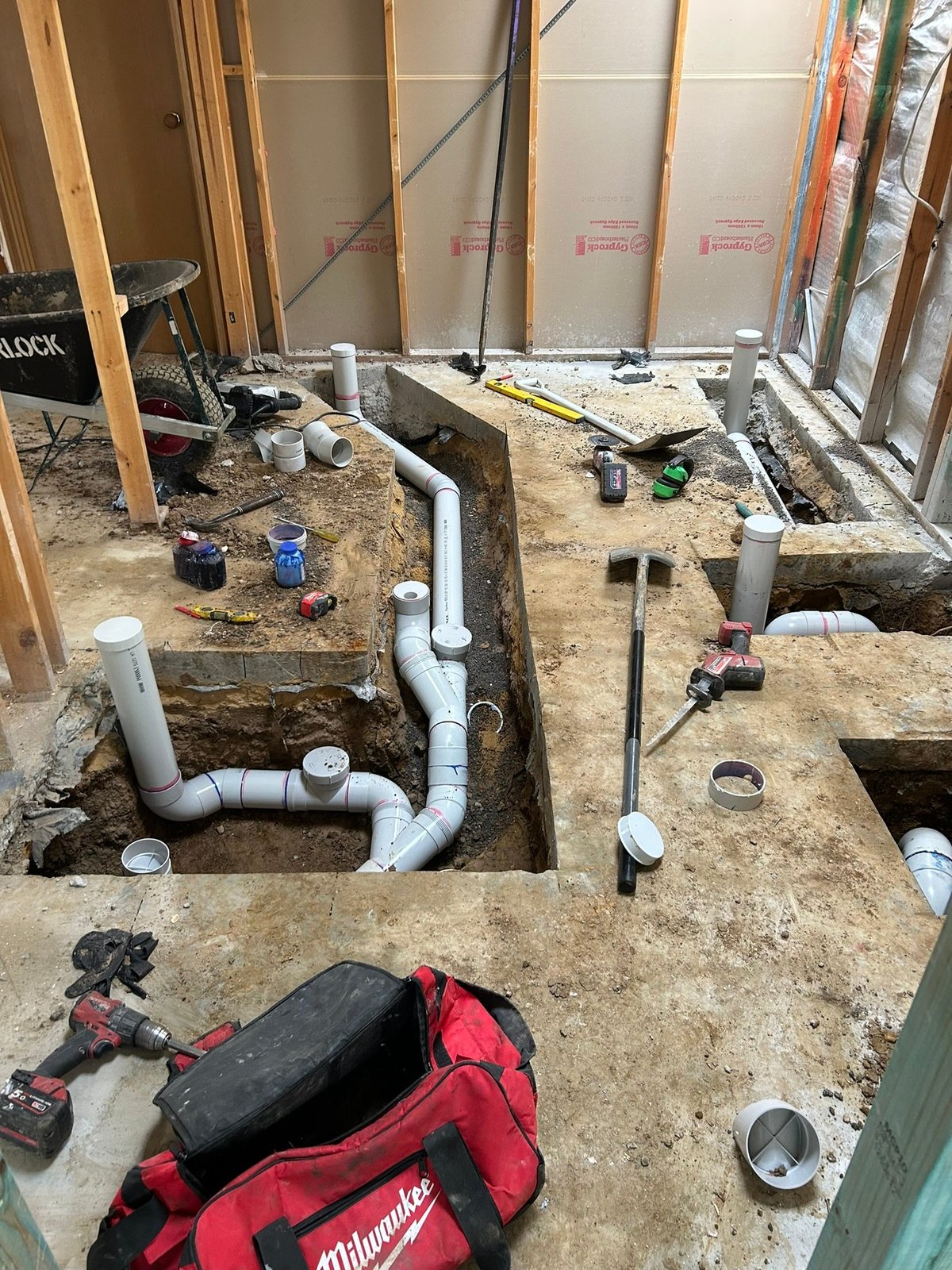 Interior construction site with PVC plumbing pipes, trenches, and Milwaukee power tools during bathroom remodel